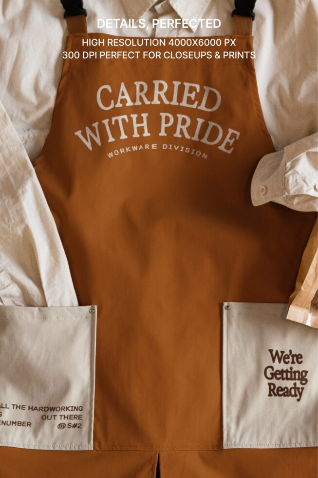 Rust apron with white text saying Carried With Pride, styled flat with shirt