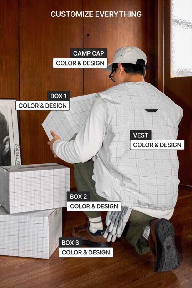 Person holding three white boxes, wearing camp cap, vest with multiple customization points
