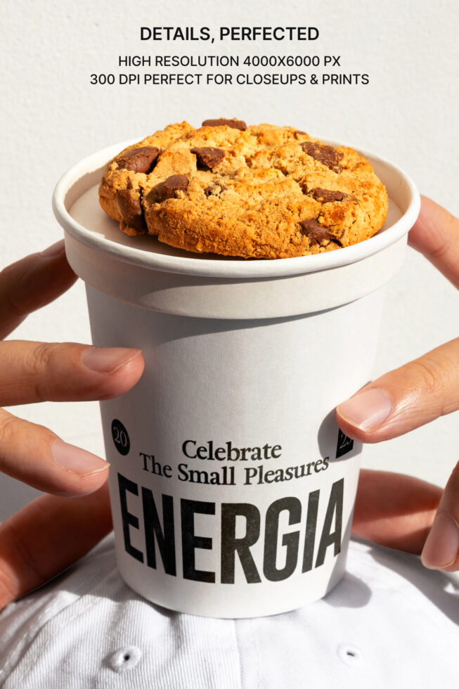 Hands holding white paper cup filled with chocolate chip cookie overhead view