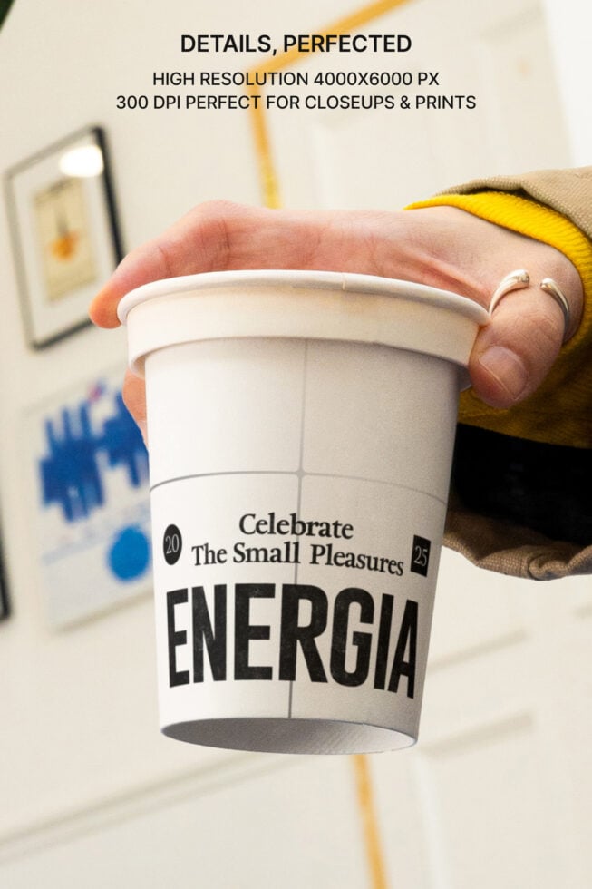 Hand holding white Energia cup with yellow sleeve against blurred background