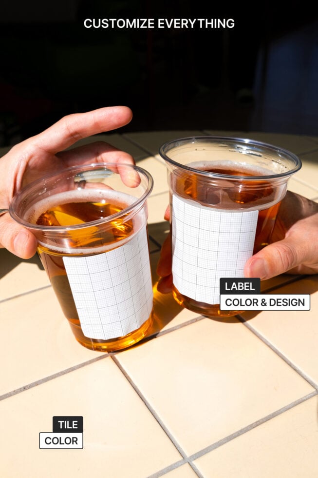Two clear cups with blank labels held in hands over tiled floor