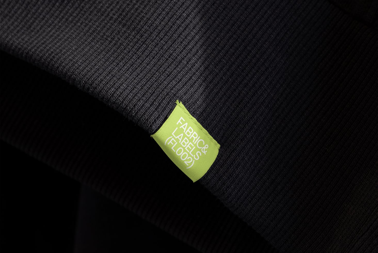 Lime green woven label tag on dark ribbed fabric texture detail shot
