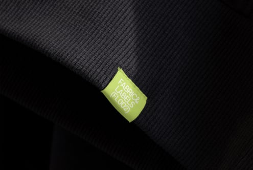 Lime green woven label tag on dark ribbed fabric texture detail shot