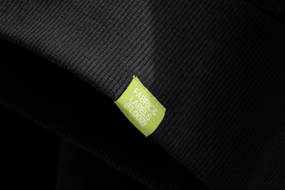 Lime green woven label tag on dark ribbed fabric texture detail shot