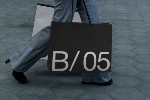 Black tote bag mockup held in hands showing B/05 typography closeup