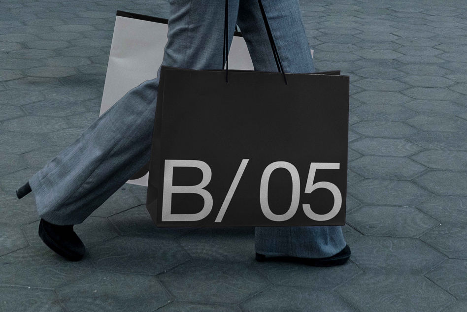 Black tote bag mockup held in hands showing B/05 typography closeup