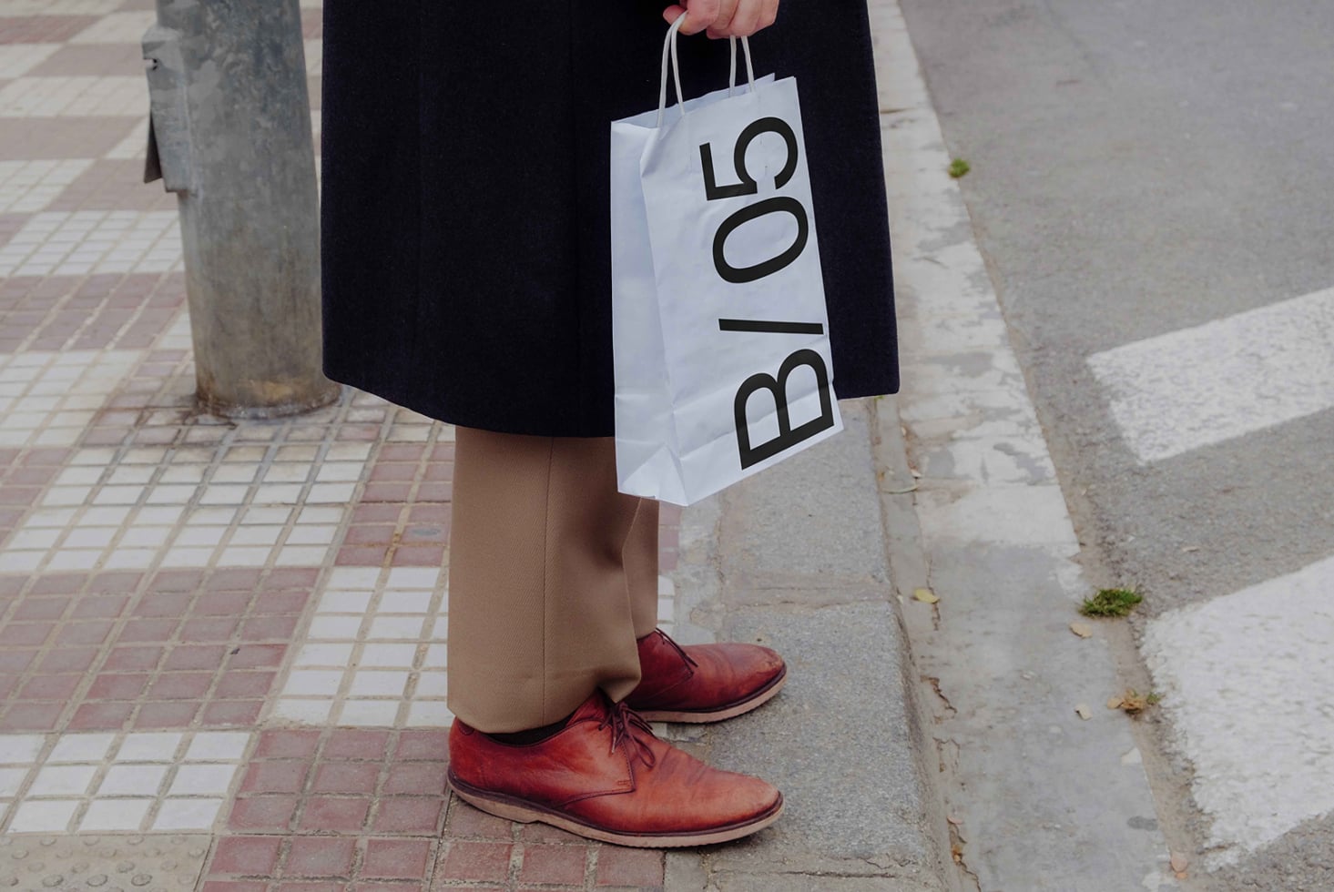 Person carrying white paper shopping bag mockup with B/05 lettering