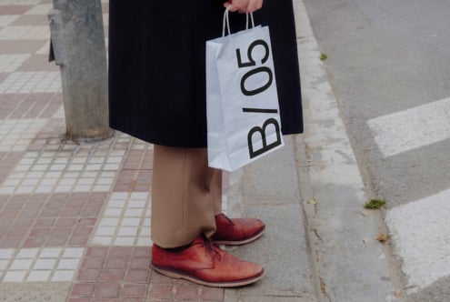 Person carrying white paper shopping bag mockup with B/05 lettering