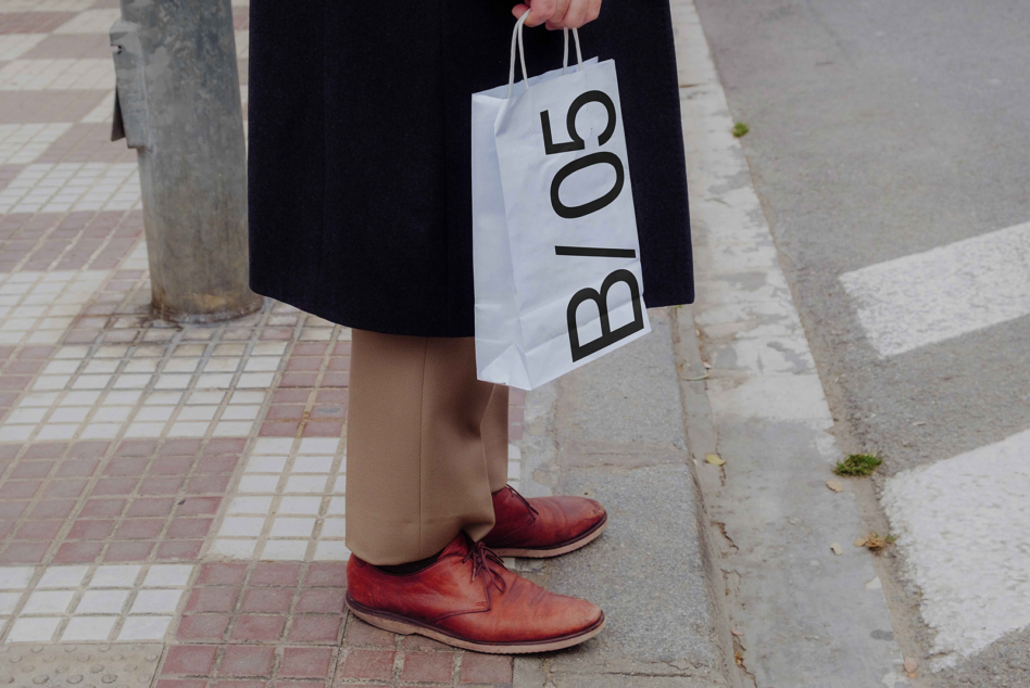 Person carrying white paper shopping bag mockup with B/05 lettering