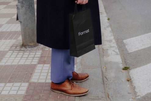 Hand holding black tote bag mockup with Format branding on street