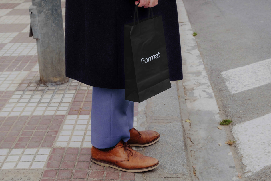 Hand holding black tote bag mockup with Format branding on street