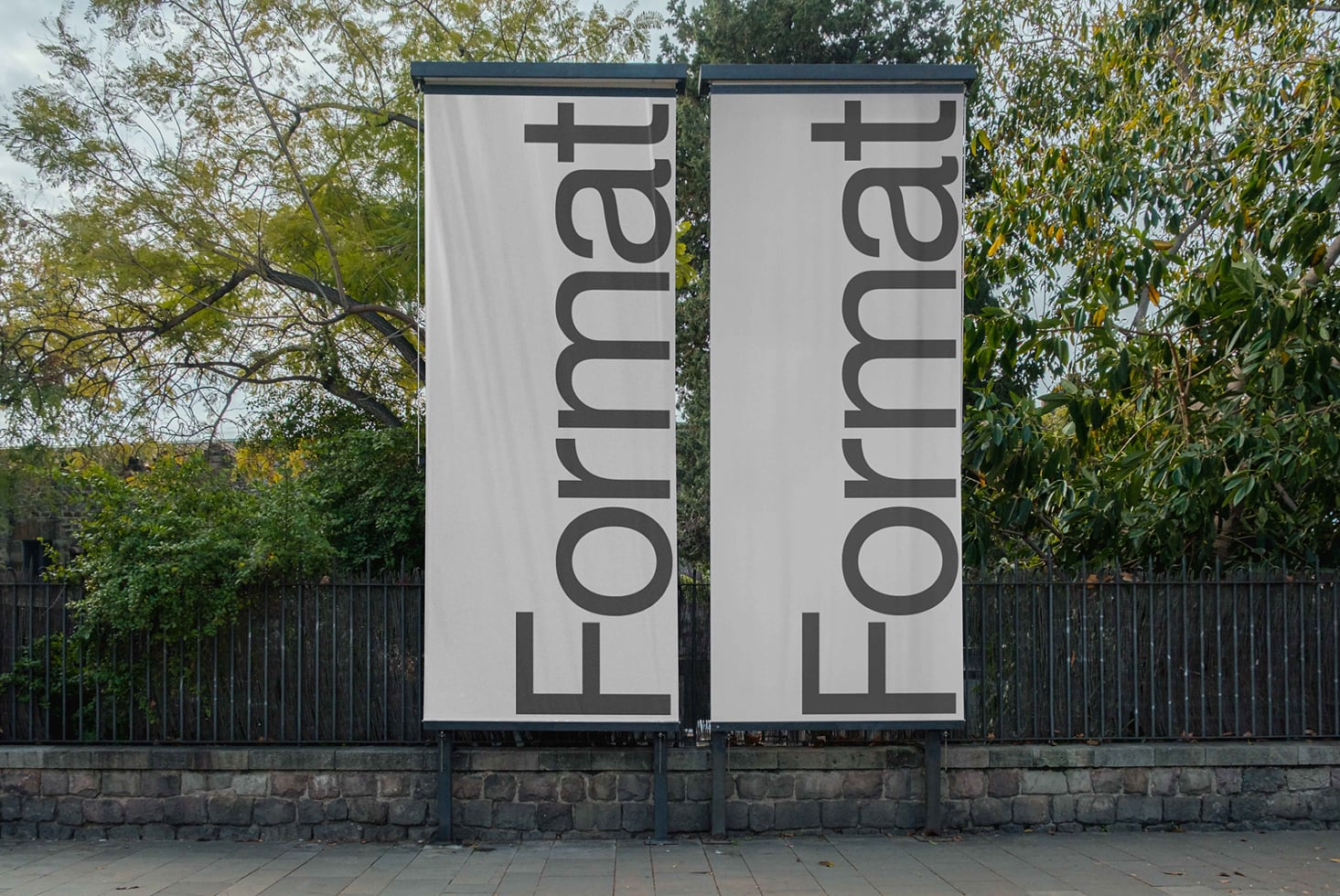 Two white vertical banners on metal frame by tree wall, gray text rotated