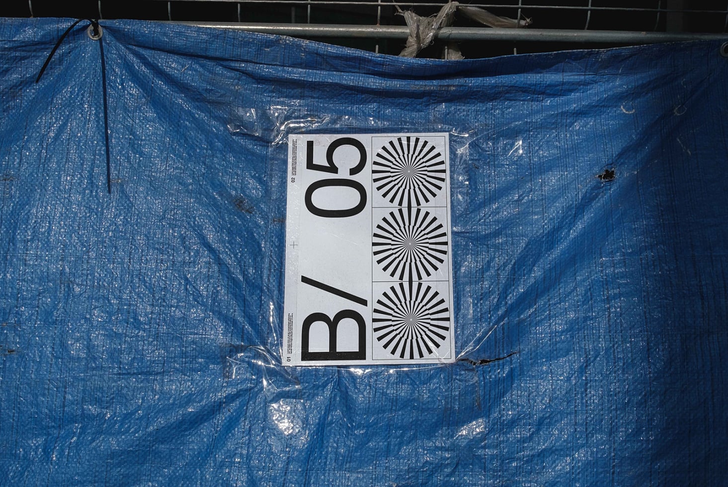 Light poster mockup hanging on blue protective material outdoors