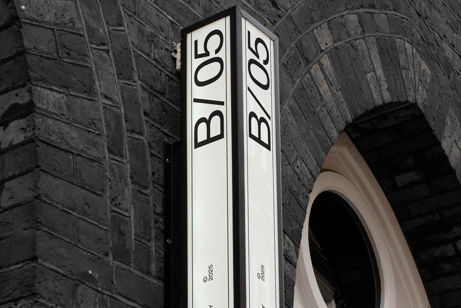 Vertical corner sign with B/05 text on stone archway with split black white panels