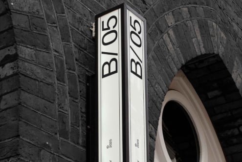 Vertical corner sign with B/05 text on stone archway with split black white panels