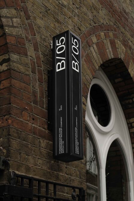 Vertical black corner sign with B/05 text mounted on red brick wall
