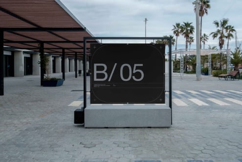Black outdoor billboard mockup on concrete plaza with palm trees in background
