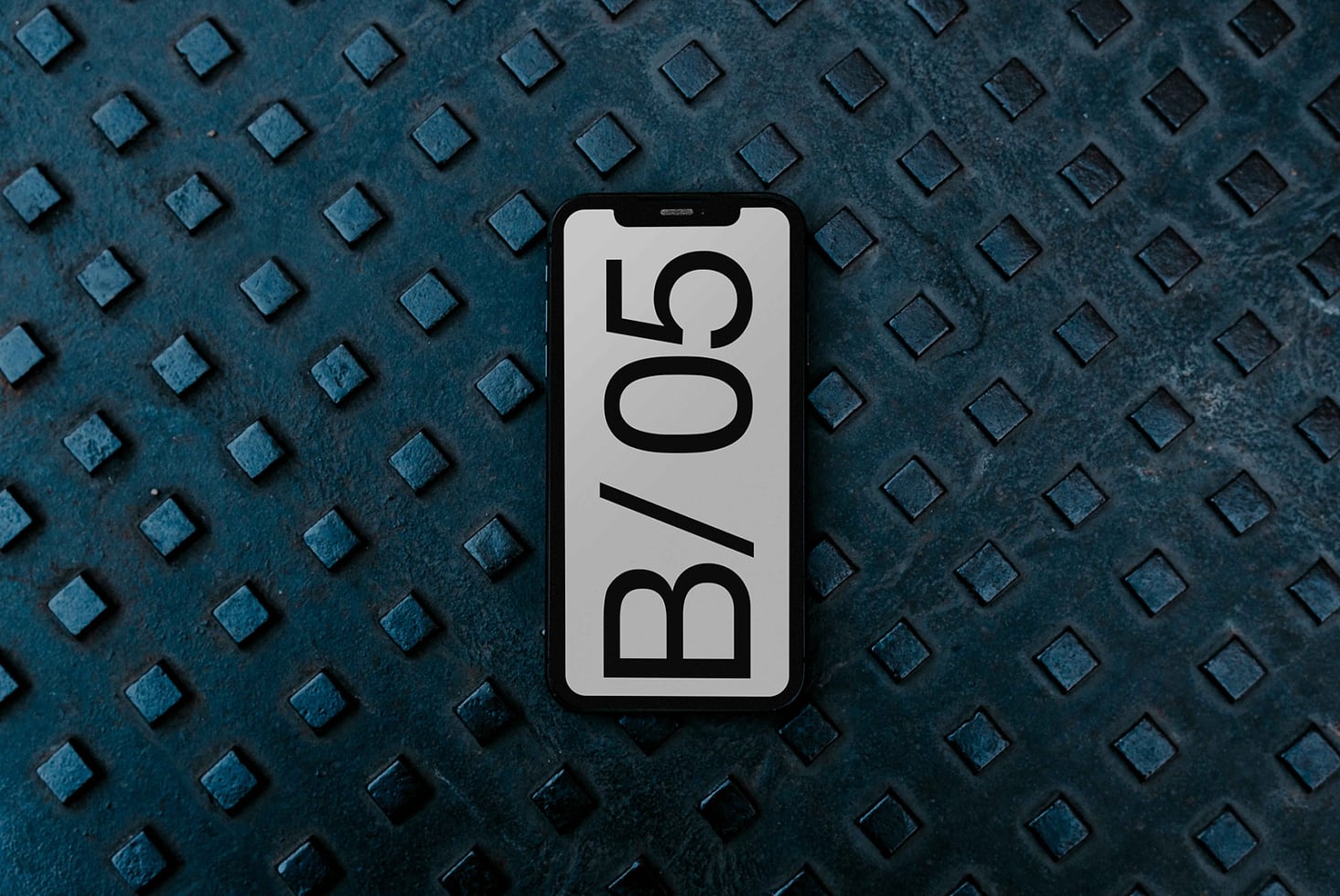 Smartphone on blue-gray diamond plate surface, white screen with B/05