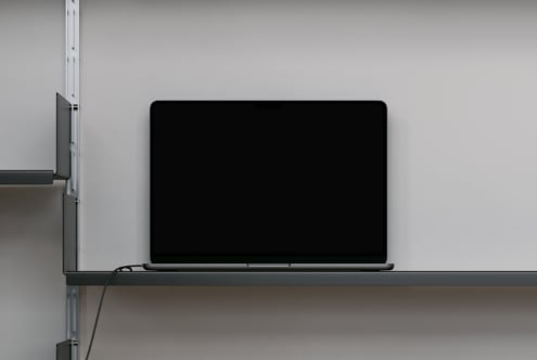 Laptop on shelf with blank black screen against light wall