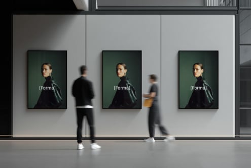 Three portrait posters in black frames on white gallery wall with people passing