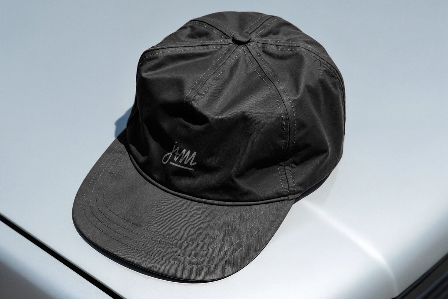 Black baseball cap with embroidered script logo on light blue background