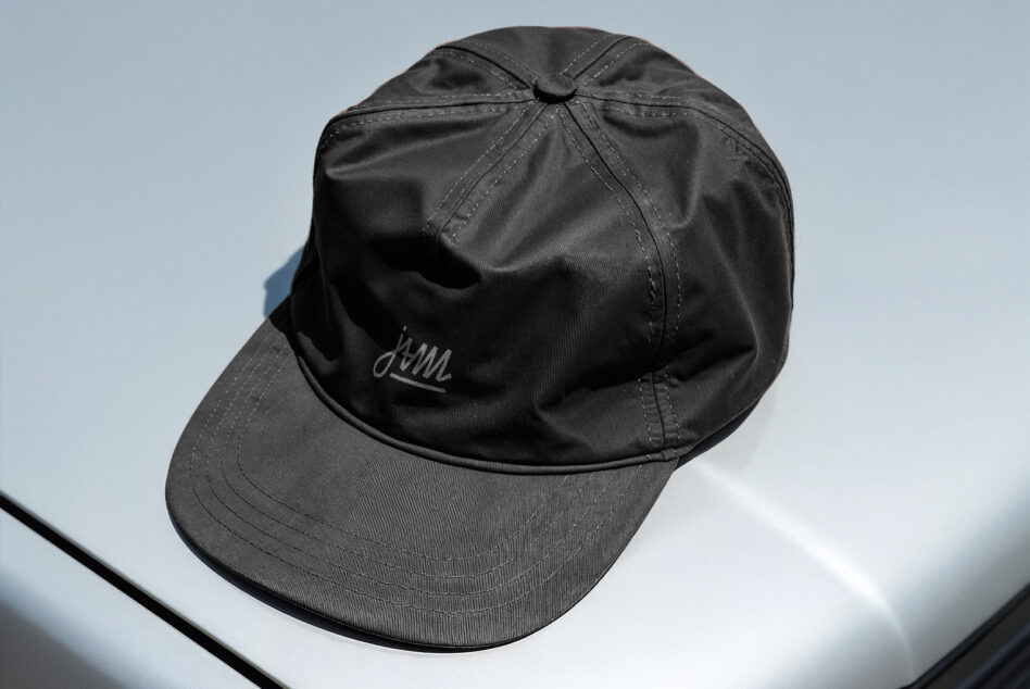Black baseball cap with embroidered script logo on light blue background
