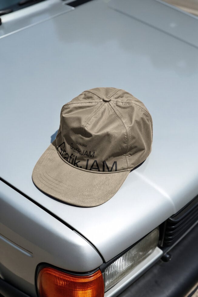 Beige baseball cap with repeating text pattern on white car hood