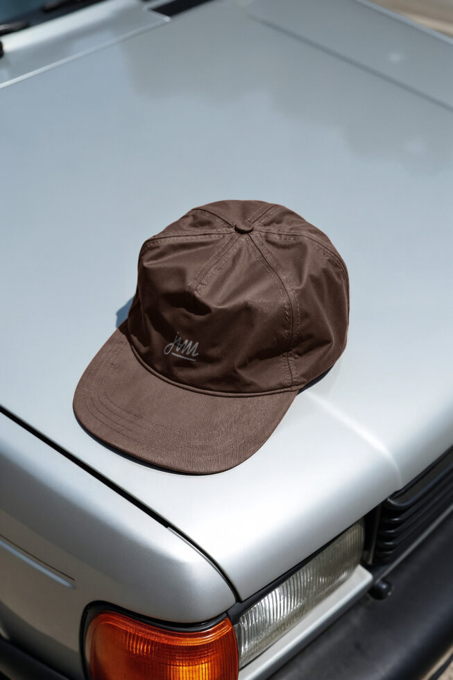 Brown baseball cap sitting on white car hood with embroidered logo