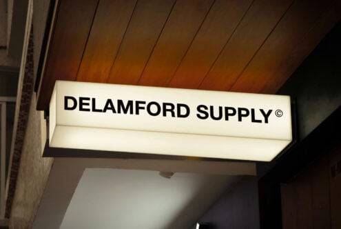 Illuminated storefront sign reading DELAMFORD SUPPLY with wood ceiling