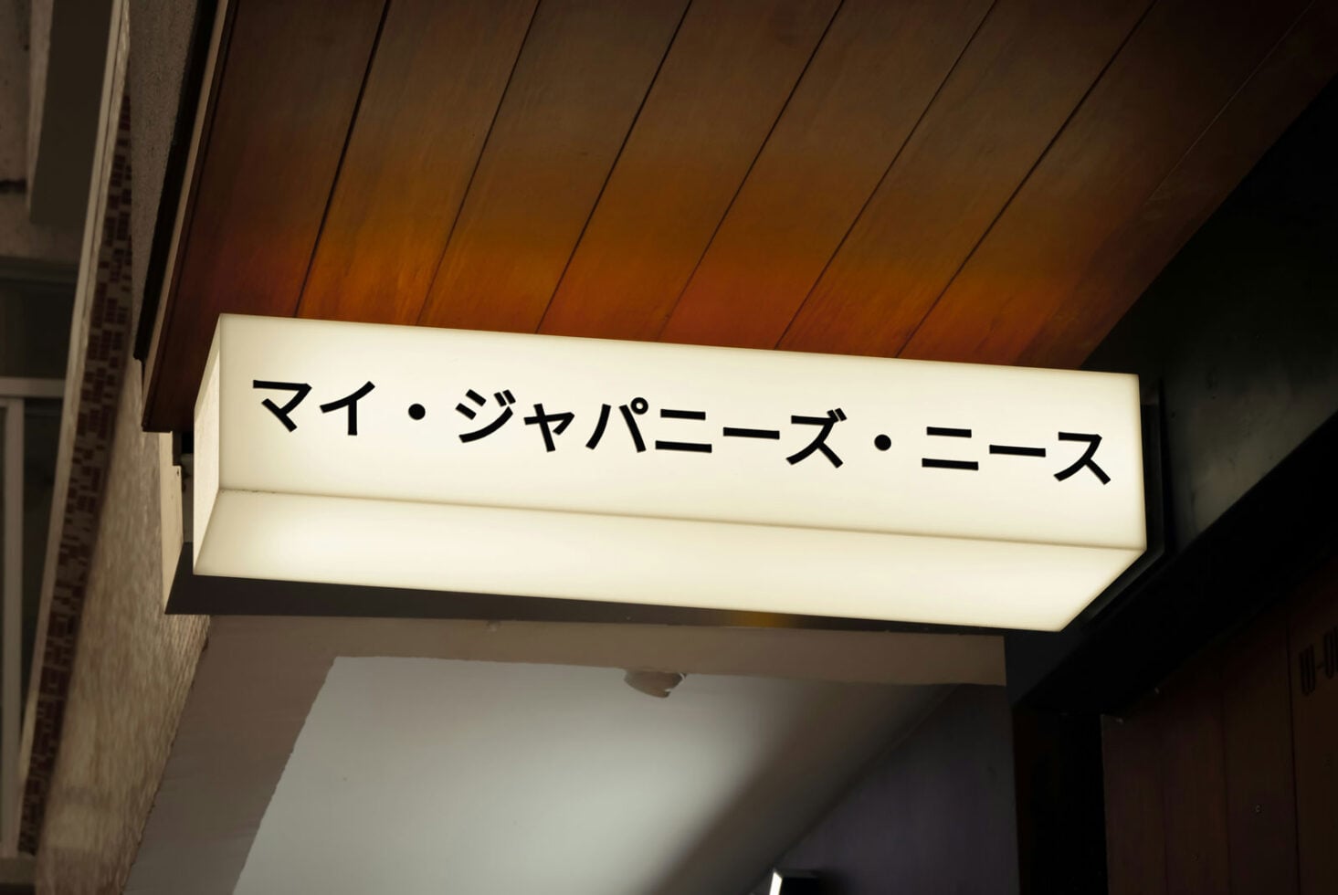 Lit ceiling sign with Japanese characters on wooden paneled background