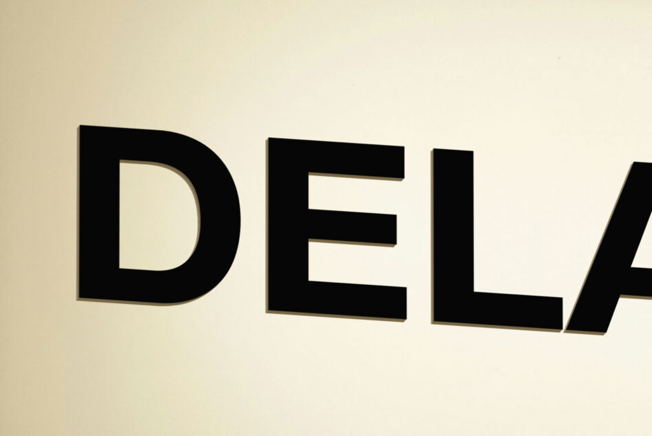 Bold black 3D letters spelling DEL on cream background with shadow
