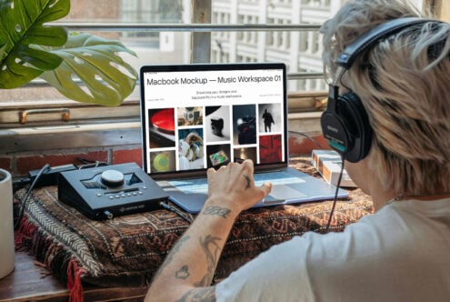 Designer in headphones reviewing MacBook Pro mockup with portfolio grid on light background workspace