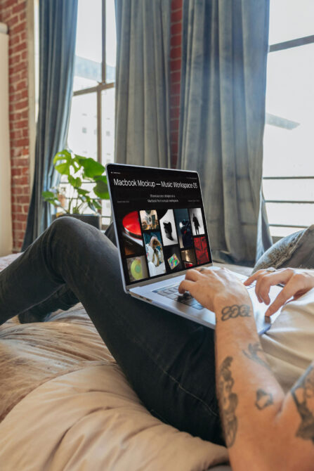 Macbook Pro displaying music workspace portfolio grid with photo layout on lap by window