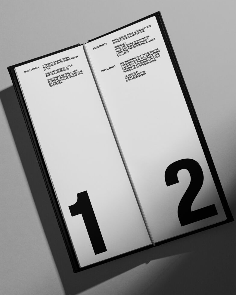 Open hardcover book with black spine on gray background showing numbered spreads