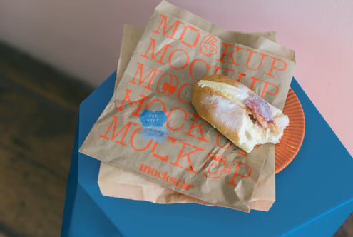 Kraft paper bag with red MOCKUP text printed on it holding sandwich on blue box