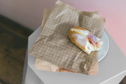 Ham sandwich on gridded kraft paper sitting on white plate with pink background