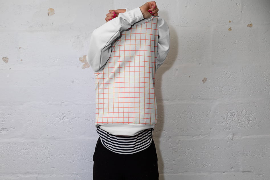 Person wearing white long sleeve with orange grid pattern tank top pulled over head