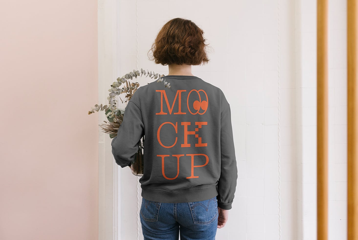 Back view of woman in charcoal sweatshirt with orange MOCK UP text holding eucalyptus