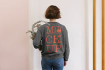 Back view of woman in charcoal sweatshirt with orange MOCK UP text holding eucalyptus