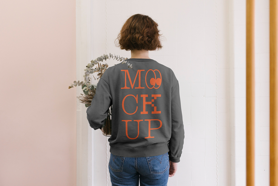 Back view of woman in charcoal sweatshirt with orange MOCK UP text holding eucalyptus