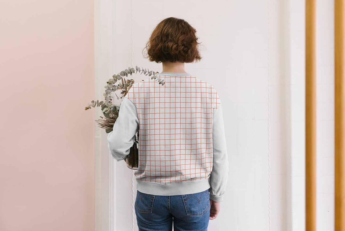 Back view of woman wearing light sweatshirt with orange grid print holding dried plants