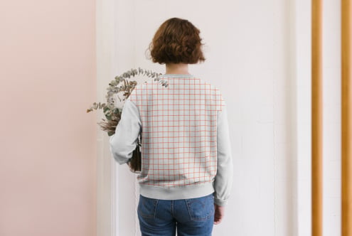 Back view of woman wearing light sweatshirt with orange grid print holding dried plants