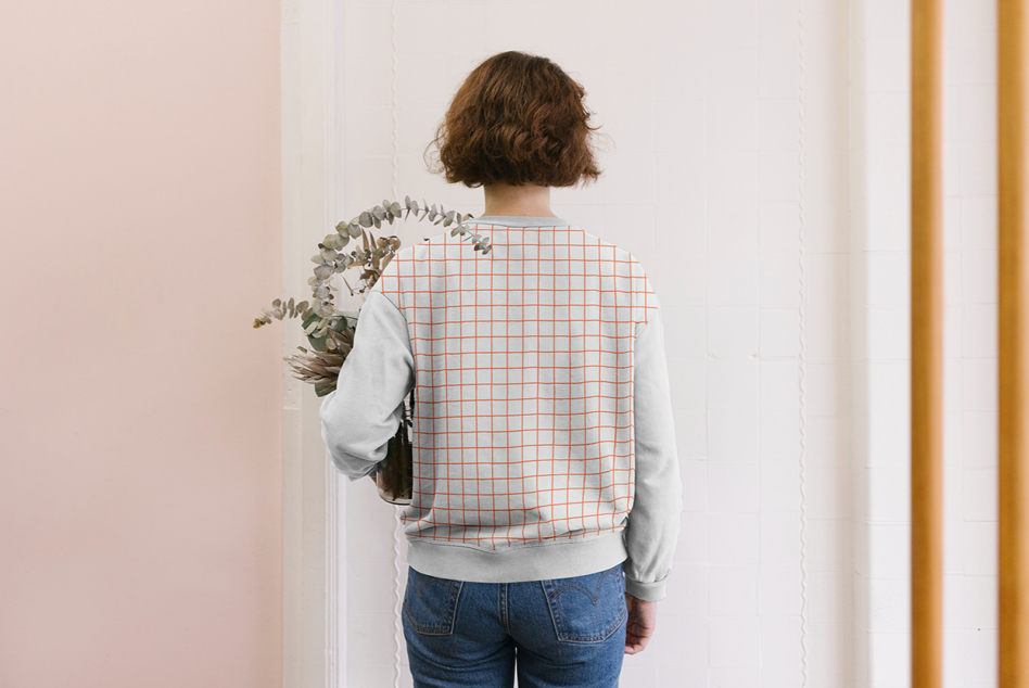 Back view of woman wearing light sweatshirt with orange grid print holding dried plants