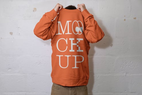 Person in orange crewneck holding it up showing back with white text