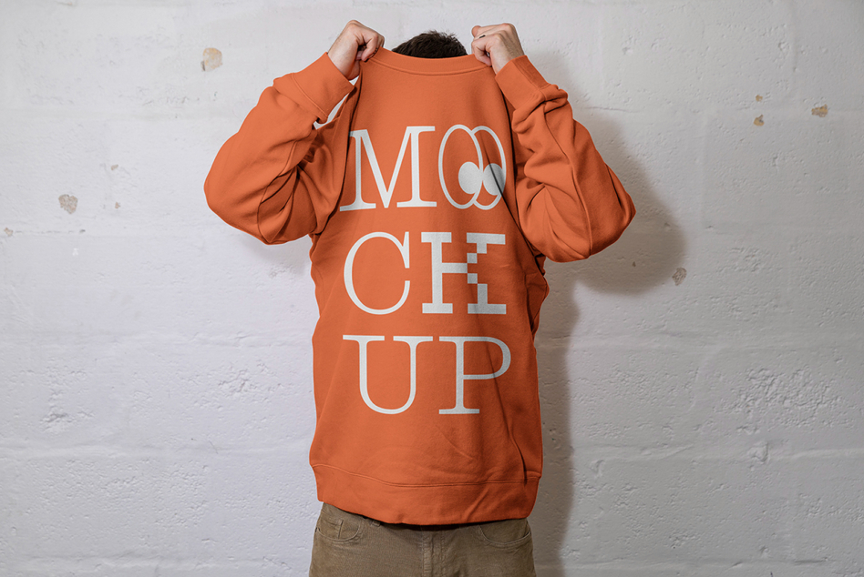 Person in orange crewneck holding it up showing back with white text