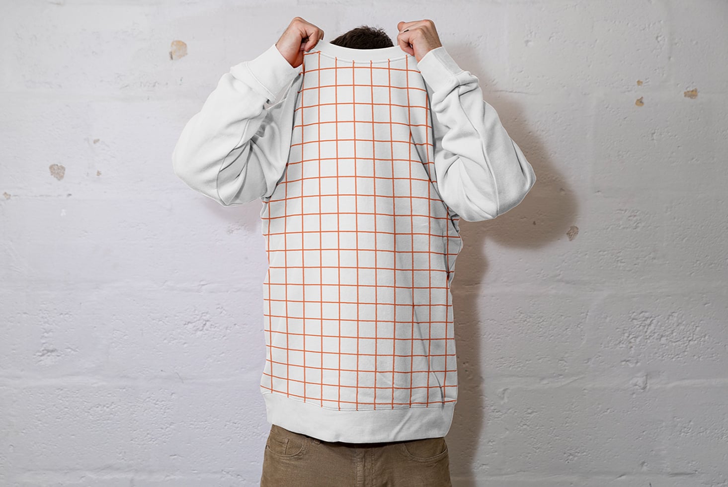 Person holding up cream crewneck sweatshirt with orange grid pattern