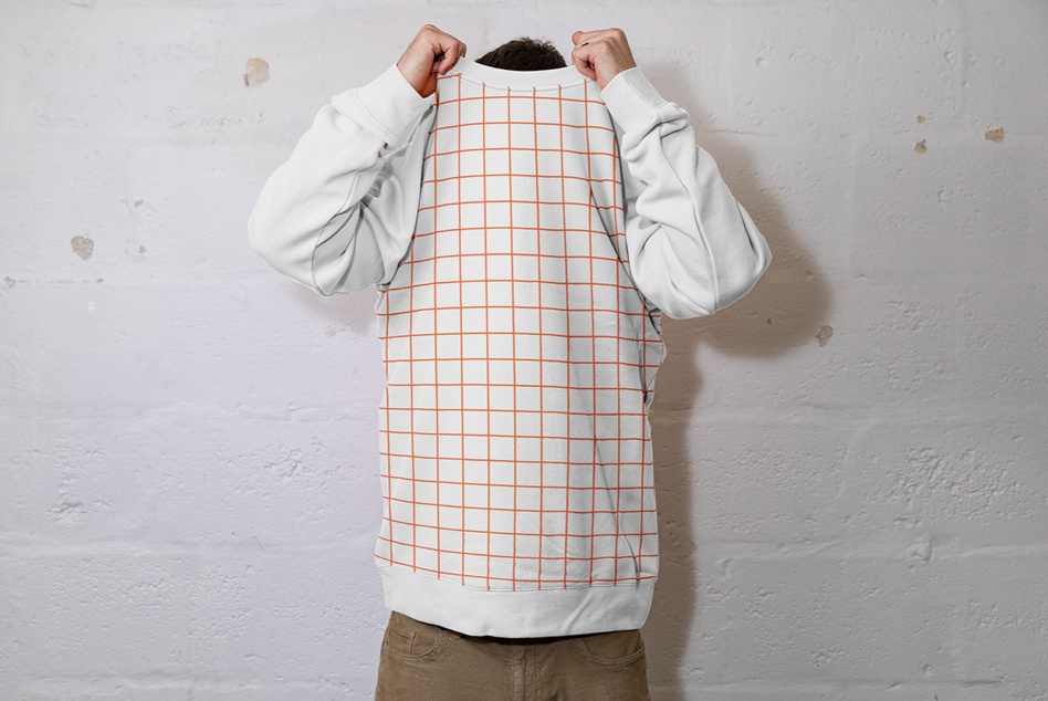 Person holding up cream crewneck sweatshirt with orange grid pattern