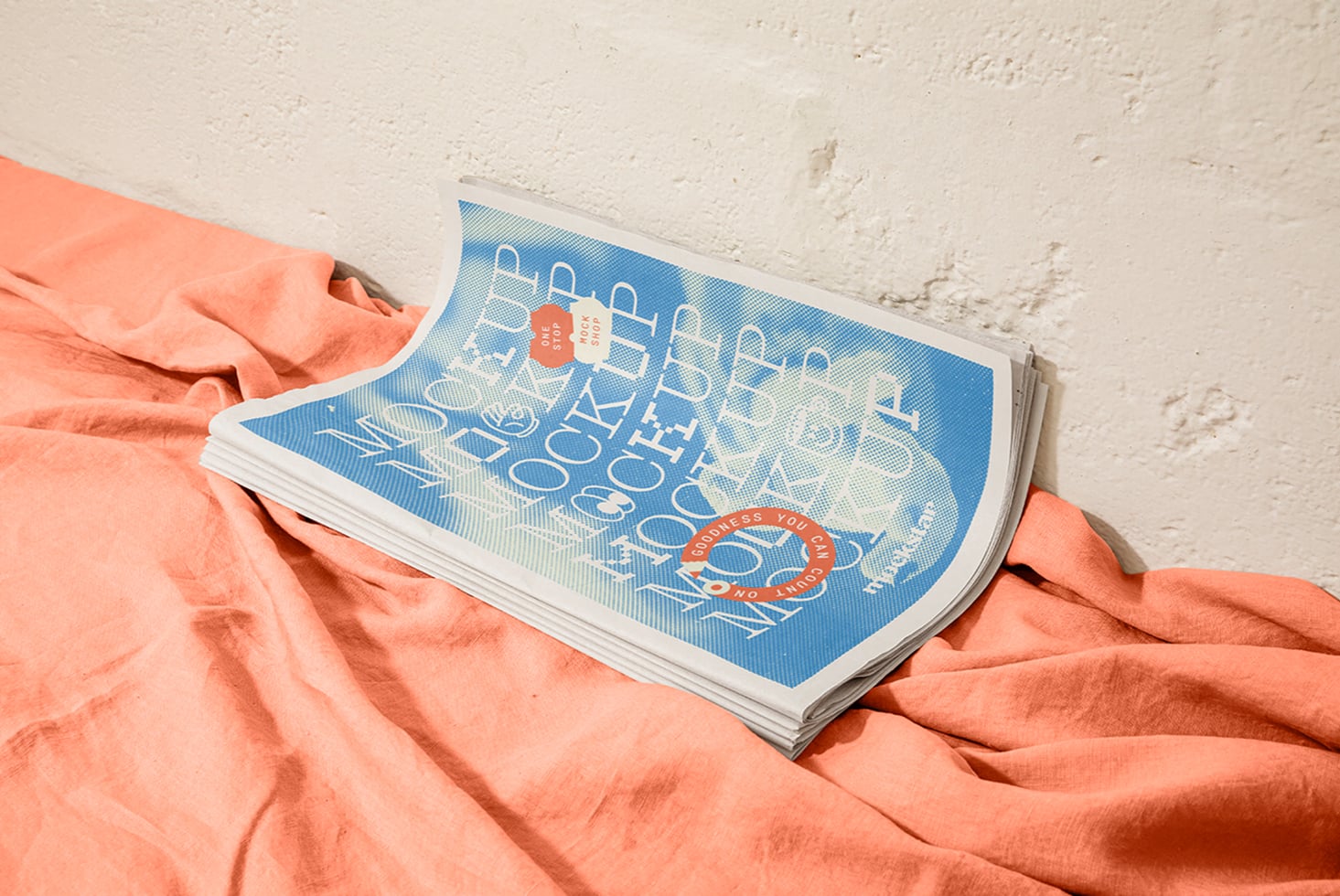 Magazine mockup with blue cover resting on coral fabric against concrete