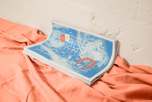 Magazine mockup with blue cover resting on coral fabric against concrete