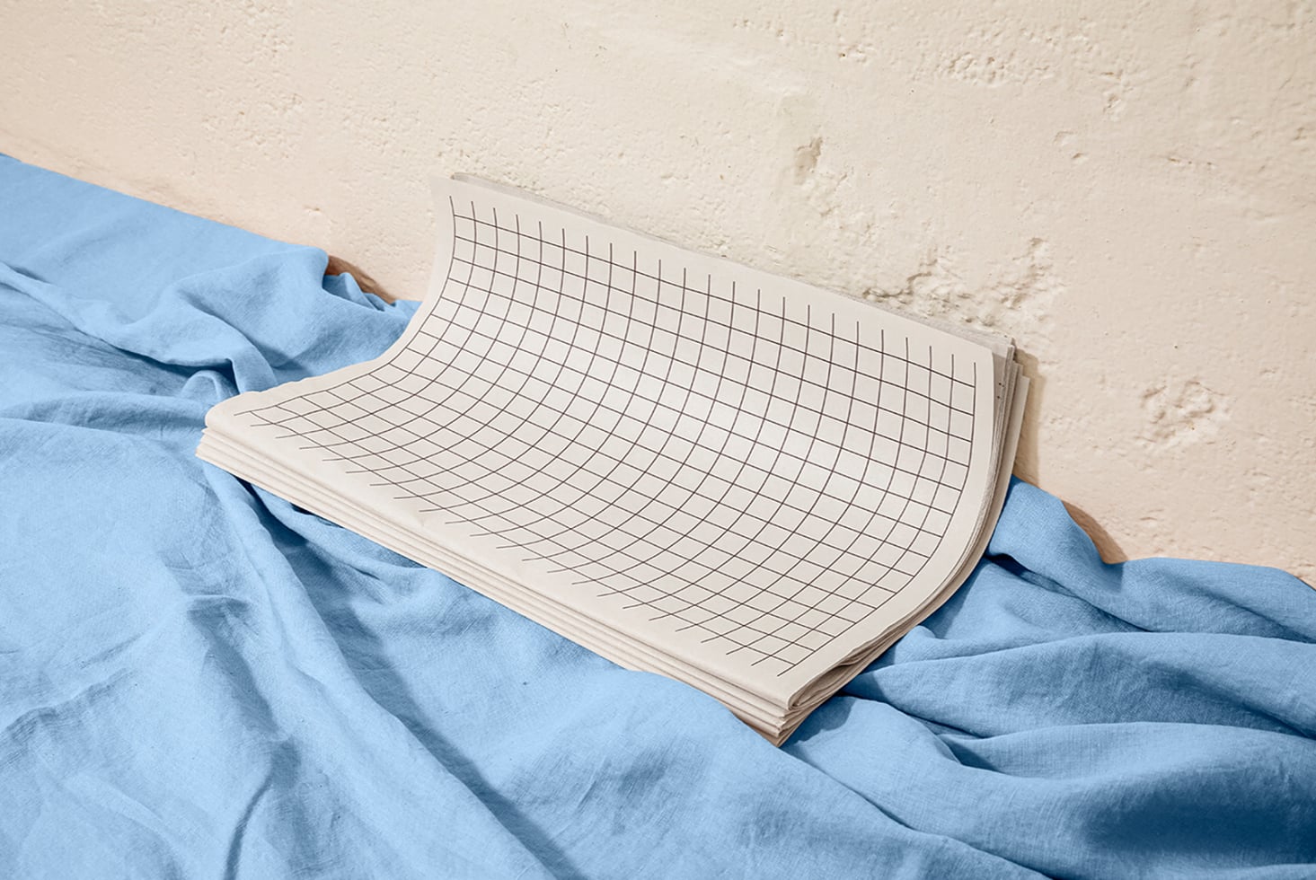 Grid notebook mockup draped over rumpled blue linen fabric